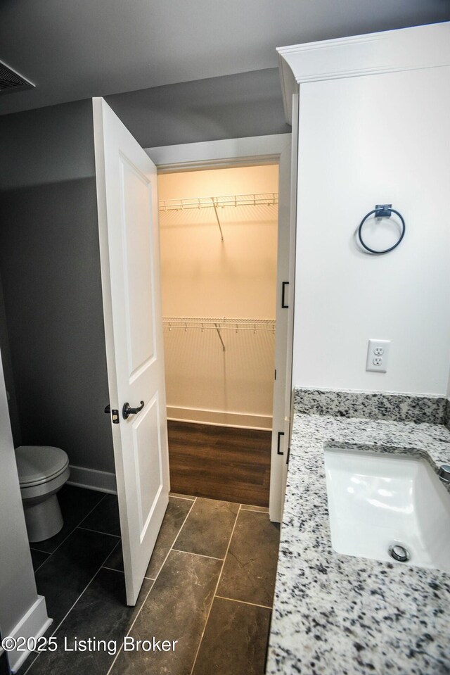 bathroom with toilet, a sink, tile patterned flooring, baseboards, and a spacious closet
