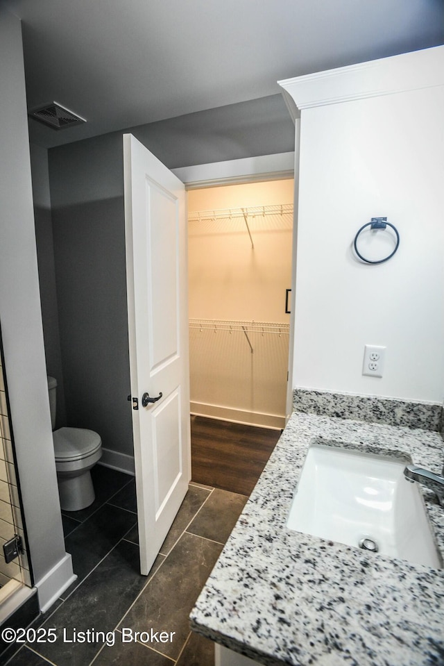 bathroom with tile patterned flooring, visible vents, a walk in closet, baseboards, and toilet