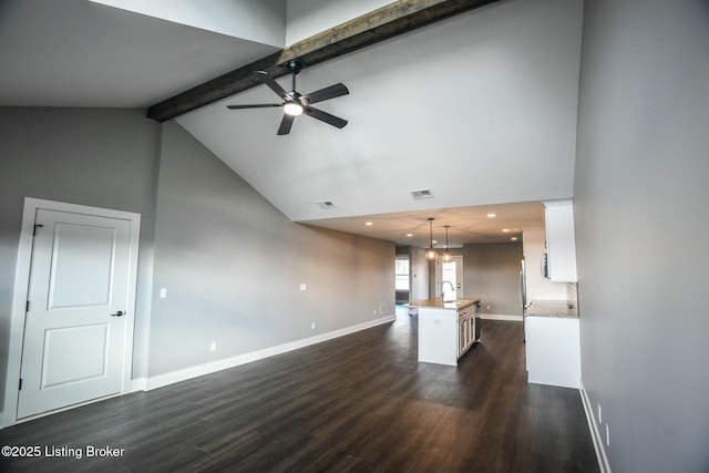 unfurnished living room with visible vents, dark wood-type flooring, beamed ceiling, and a ceiling fan