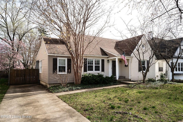 view of front of home with driveway, fence, roof with shingles, and a front yard