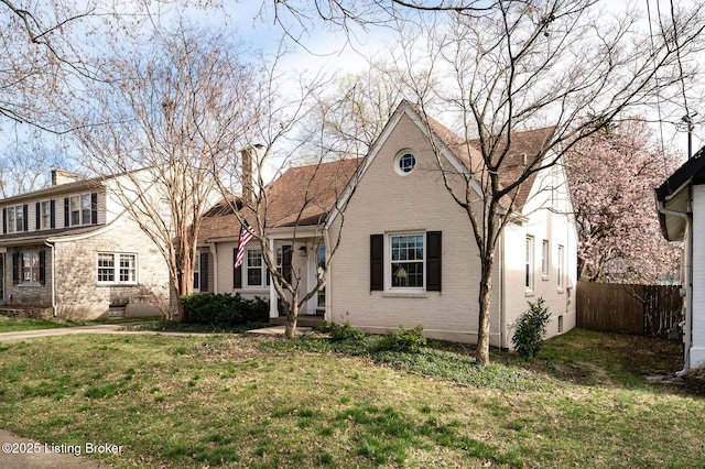 view of front of property with brick siding, a front yard, fence, and a chimney