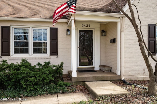 entrance to property with brick siding and a shingled roof
