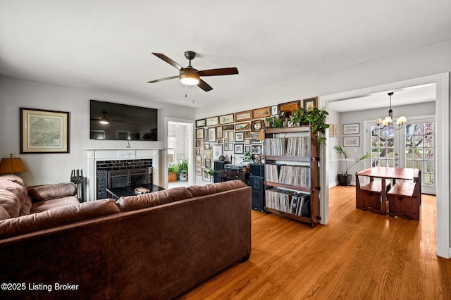 living area featuring ceiling fan with notable chandelier, wood finished floors, and a tile fireplace
