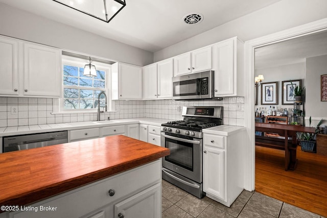 kitchen with butcher block counters, stainless steel appliances, visible vents, white cabinets, and decorative backsplash