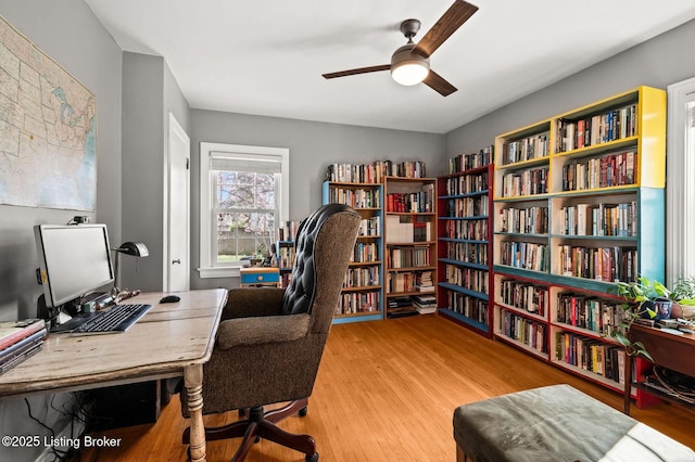 office with wood finished floors, a ceiling fan, and wall of books