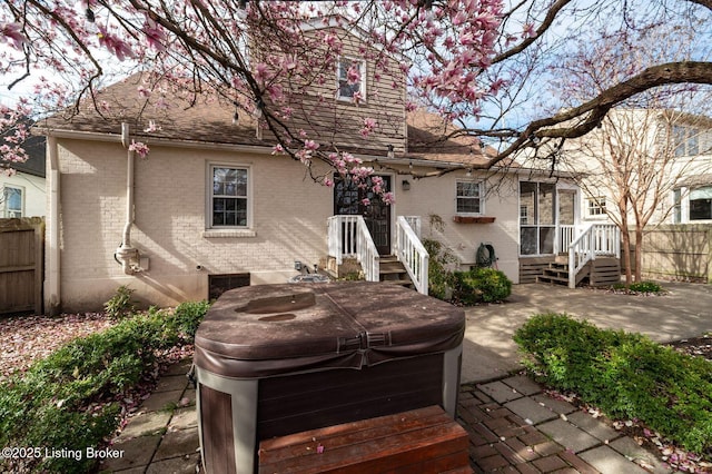 rear view of house with a hot tub, brick siding, fence, and a patio