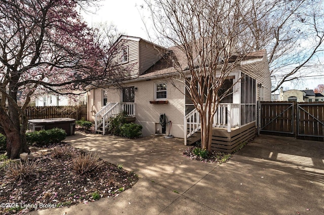 back of house with a gate, fence, a patio, brick siding, and a hot tub
