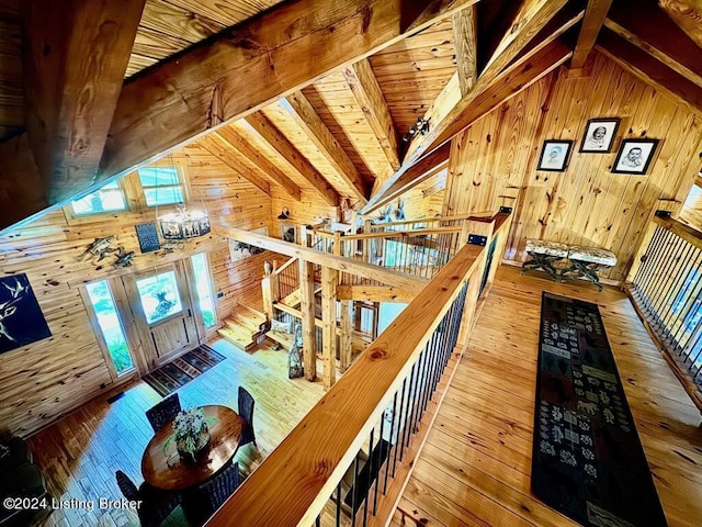 interior space featuring an upstairs landing, beamed ceiling, wood walls, high vaulted ceiling, and hardwood / wood-style floors