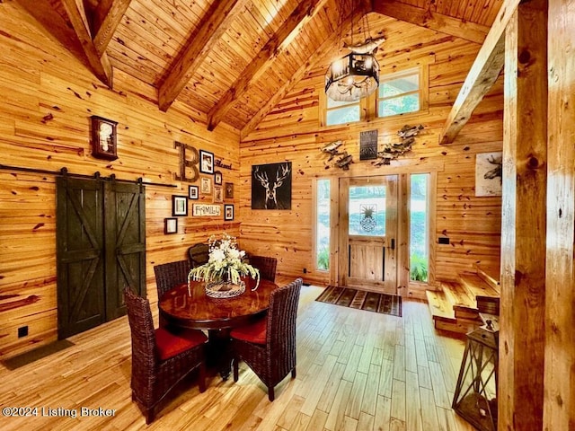 dining area featuring wood walls, light wood finished floors, a barn door, and beamed ceiling