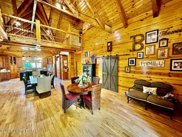dining area featuring a barn door, light wood-style flooring, wood ceiling, and wooden walls