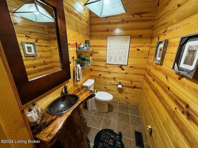half bath featuring vanity, toilet, a skylight, wood walls, and tile patterned floors