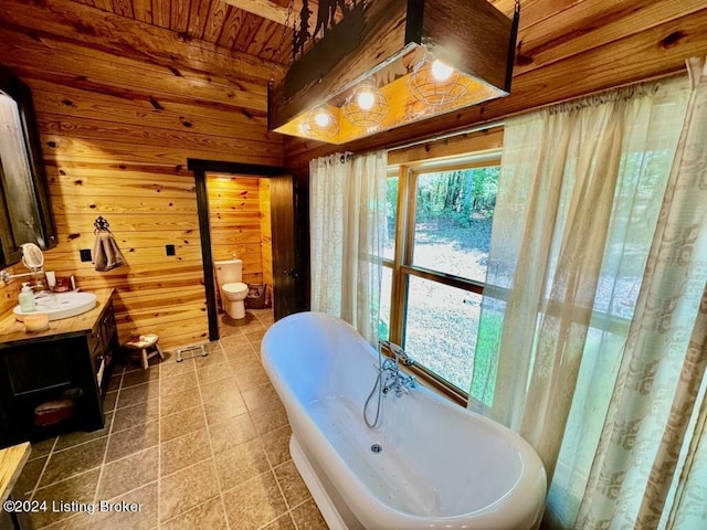 full bath featuring a freestanding tub, vanity, wooden walls, toilet, and wooden ceiling