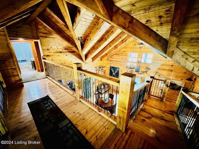 hallway featuring an upstairs landing, wood walls, vaulted ceiling with beams, and hardwood / wood-style floors