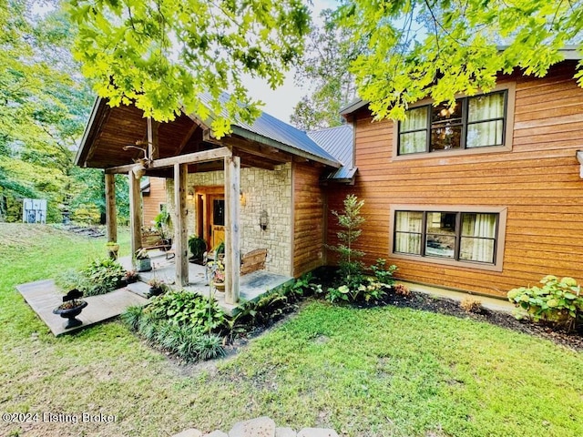 exterior space with a front yard, stone siding, metal roof, and a patio area