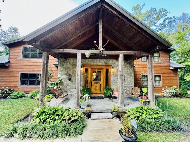 property entrance featuring a porch, stone siding, and a lawn