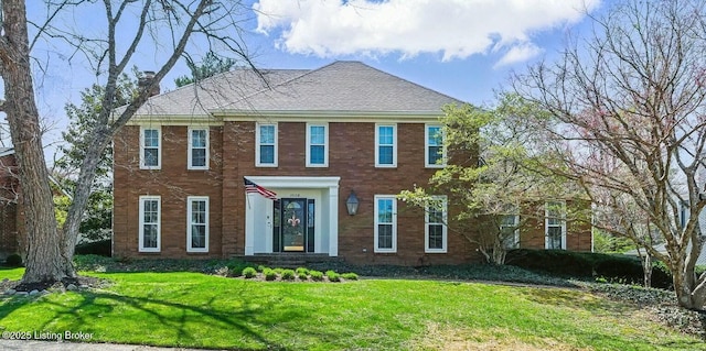 colonial-style house with brick siding, a chimney, and a front yard