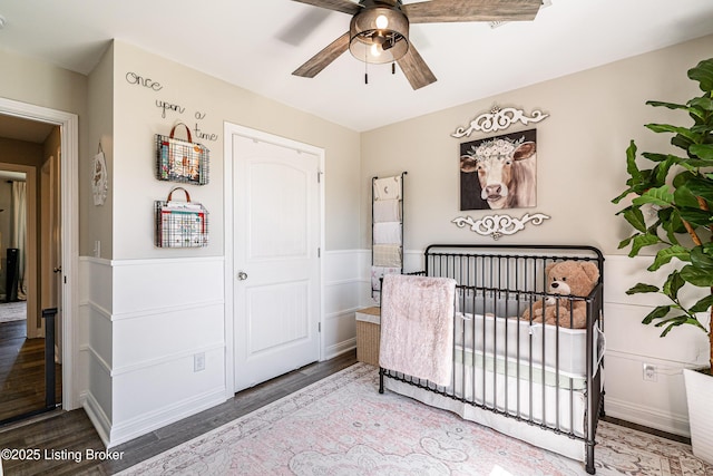 bedroom featuring ceiling fan, a crib, and wood finished floors