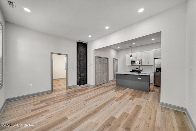 kitchen featuring white cabinets, light wood-style flooring, visible vents, stainless steel appliances, and an island with sink