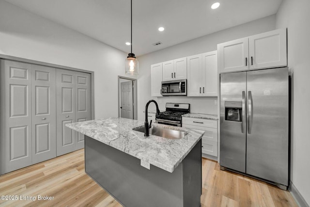 kitchen with light wood finished floors, appliances with stainless steel finishes, white cabinetry, a sink, and light stone counters