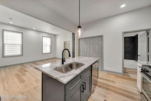 kitchen with stainless steel appliances, hanging light fixtures, a sink, light wood-style flooring, and light stone countertops