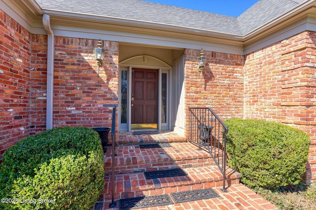 doorway to property with brick siding and a shingled roof