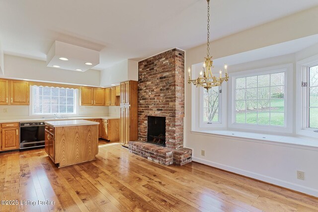 kitchen with a chandelier, light wood finished floors, light countertops, a kitchen island, and black dishwasher