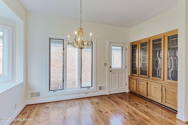 unfurnished dining area featuring baseboards, light wood finished floors, a chandelier, and visible vents
