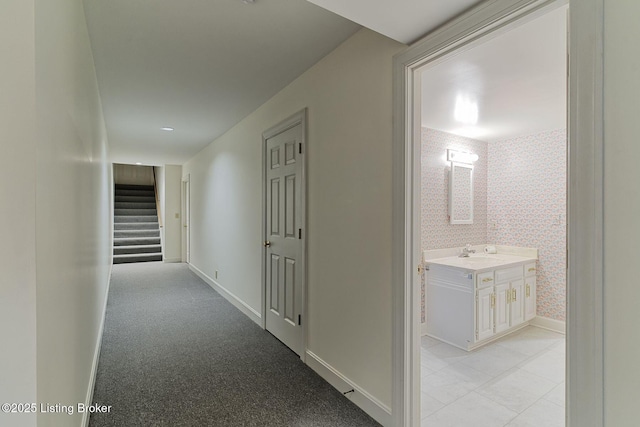 corridor featuring wallpapered walls, baseboards, a sink, and stairs