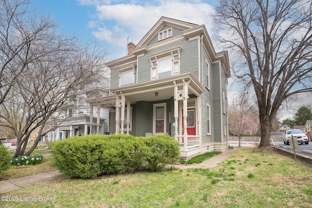 victorian-style house featuring a chimney, a front yard, and a porch