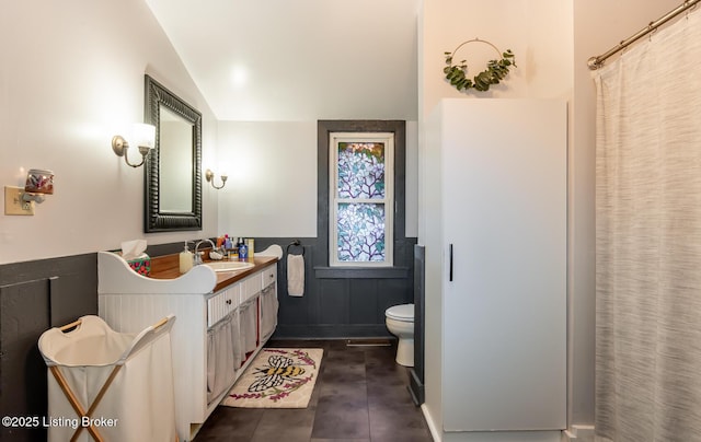 full bathroom with toilet, vaulted ceiling, vanity, and a wainscoted wall