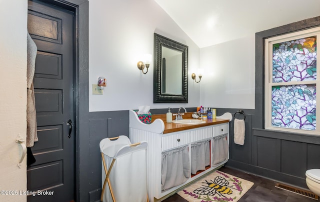 bathroom featuring a decorative wall, wainscoting, visible vents, and lofted ceiling