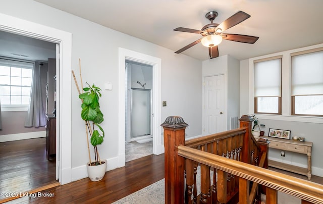 hall with visible vents, dark wood-style flooring, baseboards, and an upstairs landing