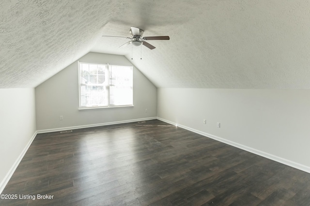additional living space featuring vaulted ceiling, dark wood-style flooring, baseboards, a textured ceiling, and ceiling fan