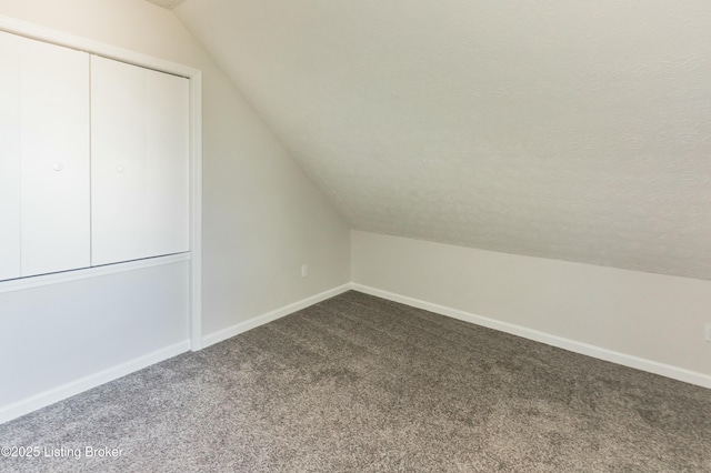 additional living space with baseboards, lofted ceiling, a textured ceiling, and dark carpet