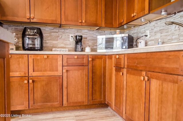 kitchen with light countertops, stainless steel microwave, backsplash, and brown cabinets