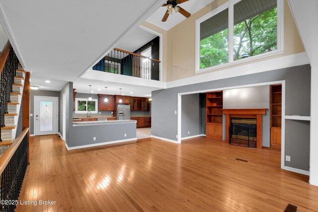 1468 Lakeshore Pkwy, Brandenburg, KY 40108 - unfurnished living room featuring stairs, a glass covered fireplace, ceiling fan, light wood finished floors, and a high ceiling