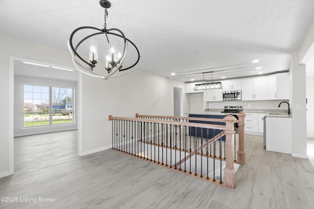 interior space featuring an upstairs landing, an inviting chandelier, baseboards, a sink, and light wood-style floors