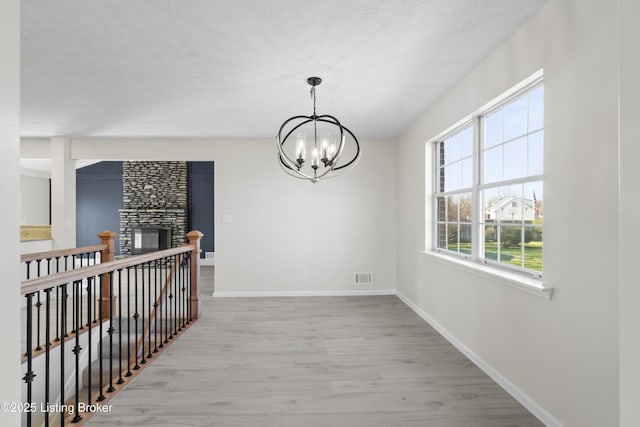 interior space featuring baseboards, visible vents, a notable chandelier, a stone fireplace, and wood finished floors