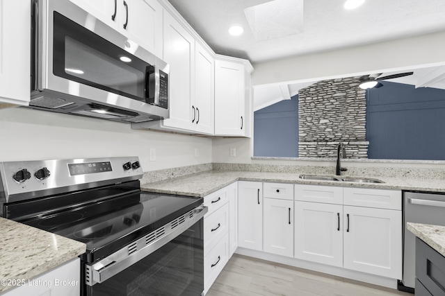 kitchen with white cabinetry, a sink, light wood finished floors, light stone countertops, and appliances with stainless steel finishes