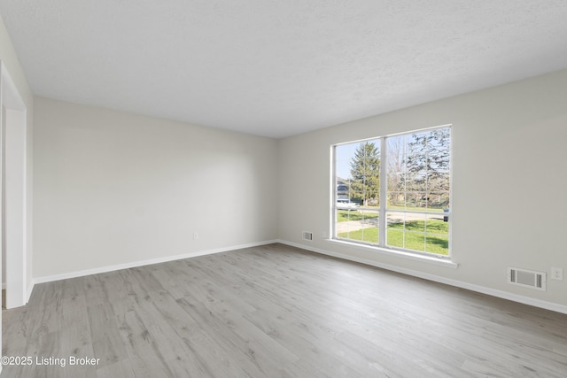 empty room with baseboards, visible vents, wood finished floors, and a textured ceiling