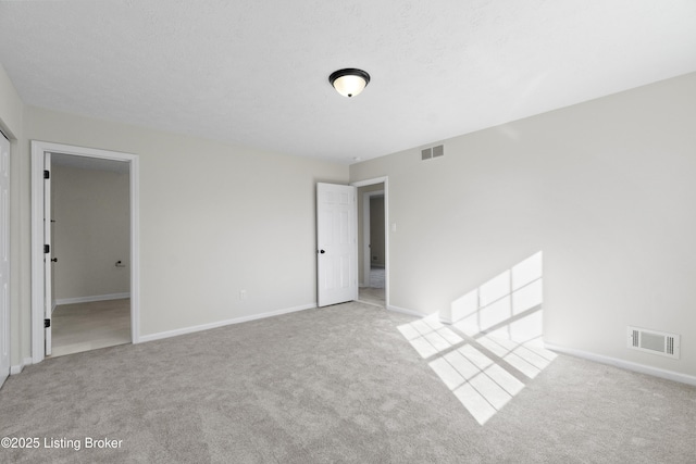 carpeted empty room featuring baseboards, a textured ceiling, and visible vents