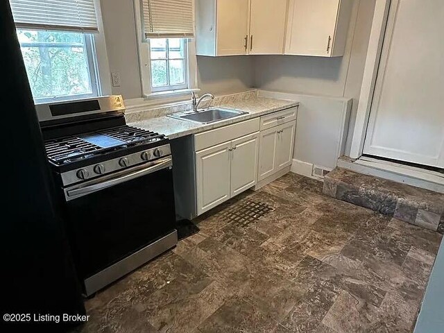 kitchen with stainless steel gas range, white cabinetry, light countertops, and a sink