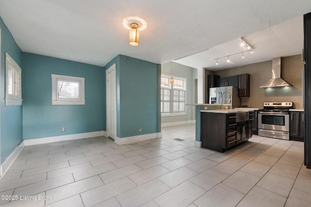 kitchen with light countertops, stainless steel appliances, baseboards, a kitchen island with sink, and wall chimney exhaust hood