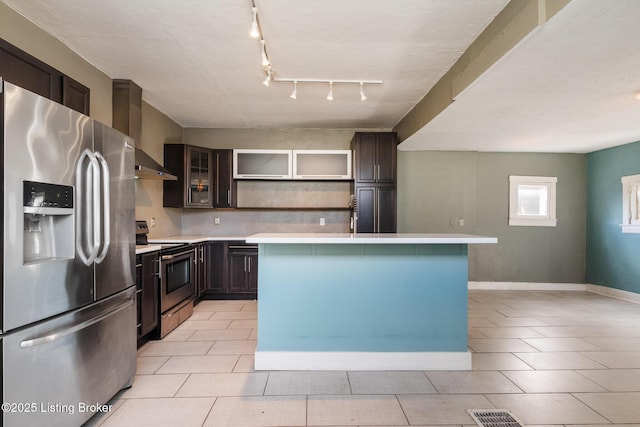 kitchen with light countertops, open shelves, wall chimney exhaust hood, stainless steel appliances, and dark brown cabinets