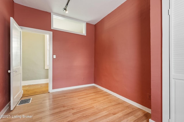 unfurnished room with baseboards, visible vents, light wood-style flooring, and rail lighting