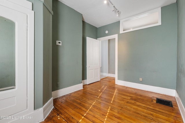 empty room with baseboards, visible vents, rail lighting, and wood-type flooring
