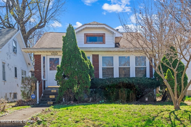bungalow with brick siding, a front yard, and roof with shingles