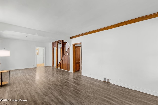 unfurnished living room with baseboards, visible vents, wood finished floors, and arched walkways