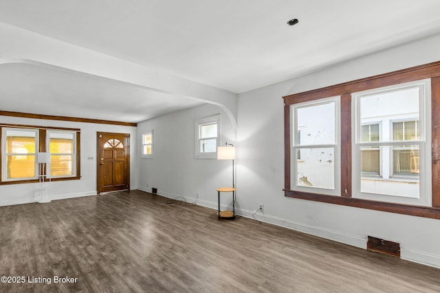 unfurnished living room with dark wood-type flooring, visible vents, arched walkways, and baseboards