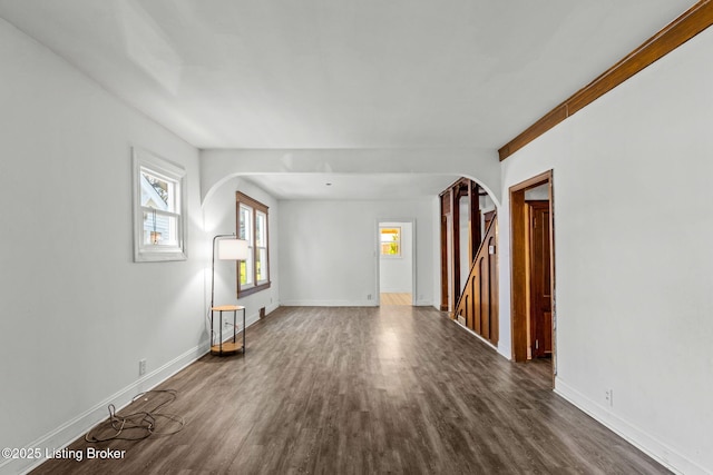 empty room featuring arched walkways, baseboards, and dark wood-type flooring